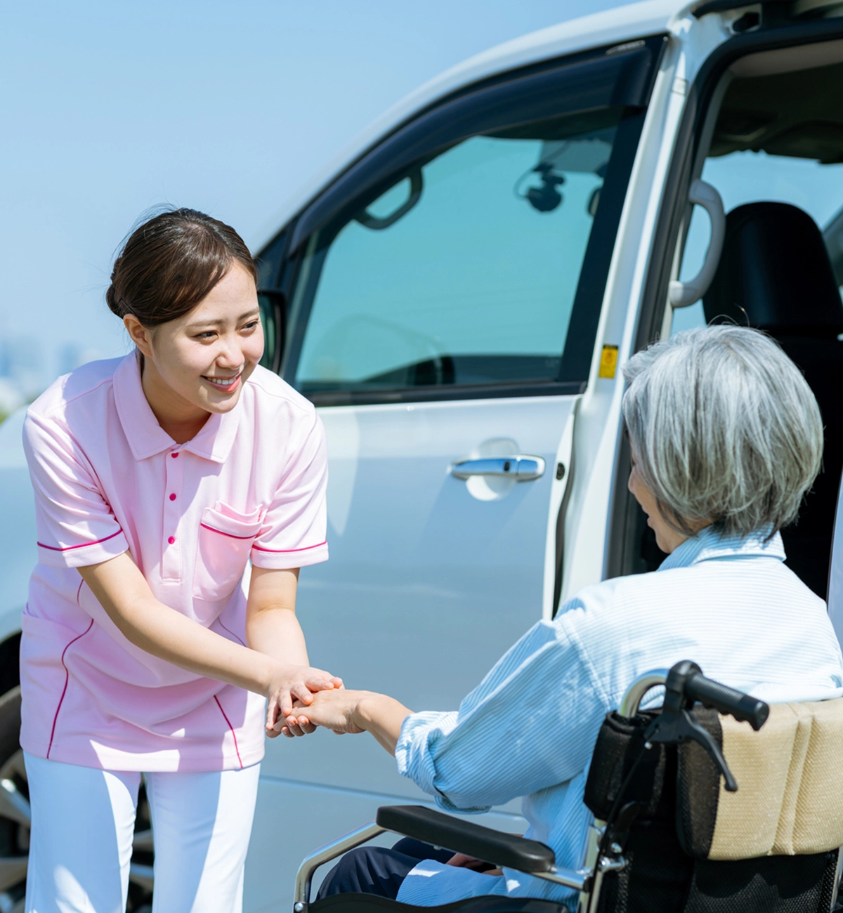 Caregiver assisting elderly person from vehicle.
