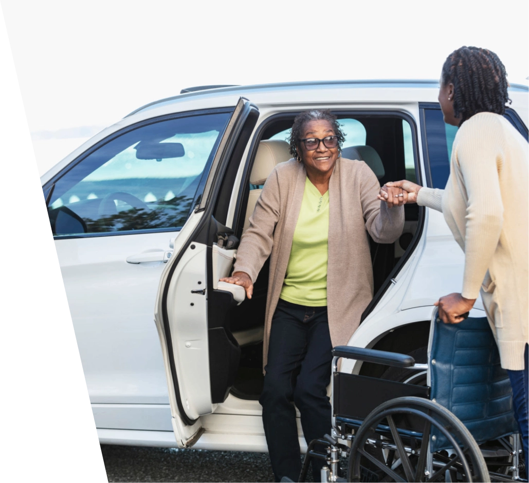 Woman assists another exiting car to wheelchair.