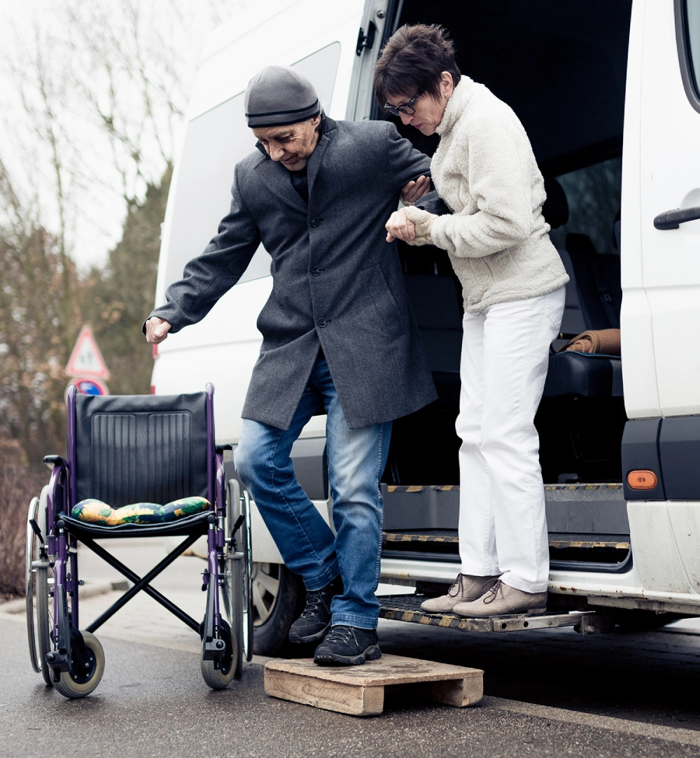 Person assisting another from van to wheelchair.